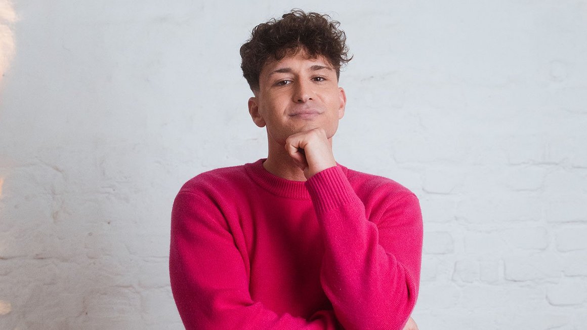 Muškarac u ružičastom džemperu zamišljeno gleda u kameru