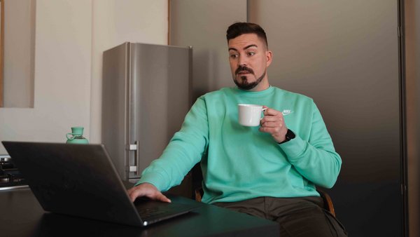 Osiguranje vašeg automobila Čovjek sjedi ispred laptopa sa šalicom u ruci, šokiran.