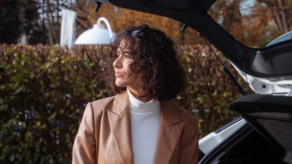 Mlada žena stoji ispred otvorenog prtljažnika svog automobila