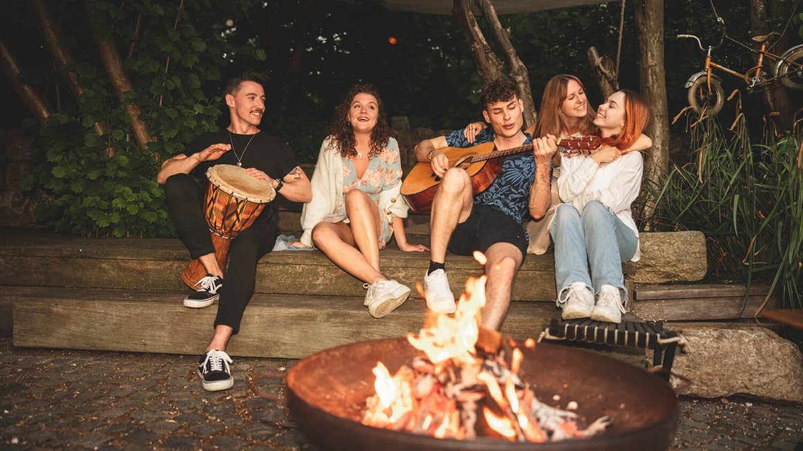 Mladi ljudi sjede oko logorske vatre – avantura života u kamperu
