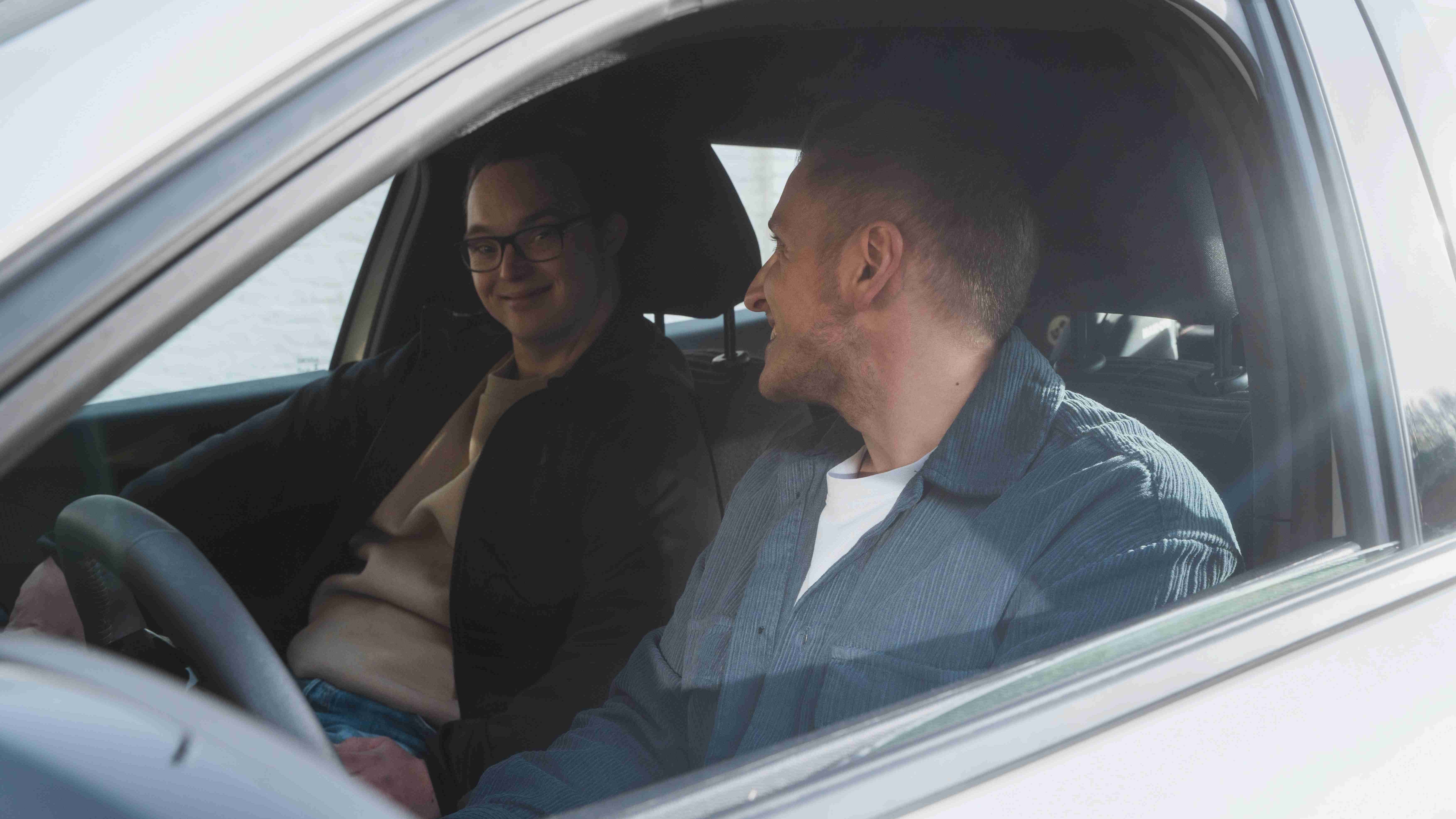 Dvoje mladih ljudi sjede u automobilu i smiješe se jedan drugome